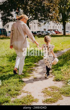 Donna anziana che tiene per mano la nipote che cammina al parco Foto Stock