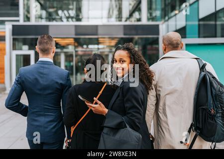 Ritratto laterale di una donna d'affari sorridente che guarda a spalla con i colleghi di fronte all'edificio Foto Stock