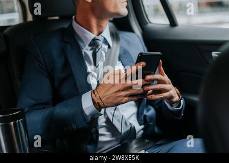 Parte centrale di un uomo d'affari che tiene uno smartphone mentre è seduto in auto Foto Stock