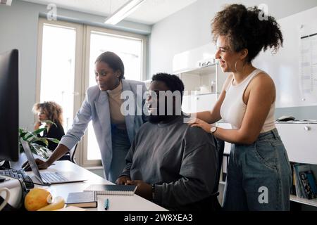 Collega felice che incoraggia un dipendente di sesso maschile seduto alla scrivania in ufficio Foto Stock