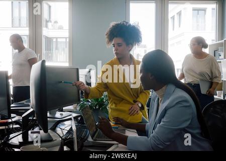 Donna d'affari che spiega la codifica a una collega seduta alla scrivania in ufficio Foto Stock