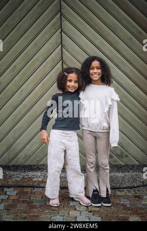 Ritratto di sorelle sorridenti in piedi con le braccia di fronte al muro Foto Stock