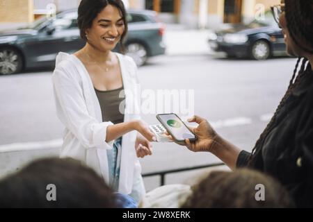 Una donna sorridente che prende il pagamento online dal cliente mentre vende sul mercato Foto Stock