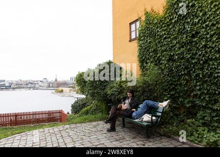 Amiche femminili che parlano tra loro in panchina vicino alle piante al parco Foto Stock