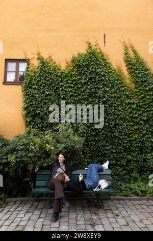 Giovani amiche che trascorrono il tempo libero in panchina vicino alle piante del parco Foto Stock