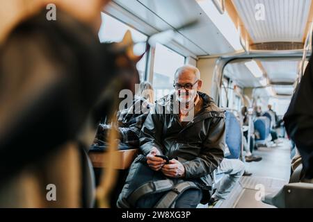 Uomo anziano che usa uno smartphone e si siede in autobus mentre viaggia per lavoro Foto Stock
