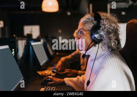 Vista laterale di una donna anziana che gioca a videogiochi sul computer nel centro giochi Foto Stock