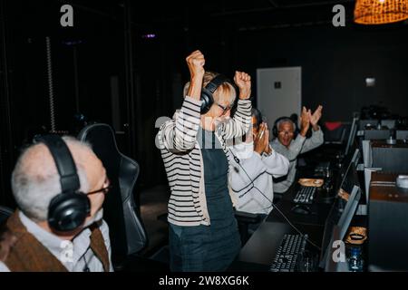 Donna anziana che festeggia la vittoria di amici maschi e femmine nella sala giochi durante il fine settimana Foto Stock