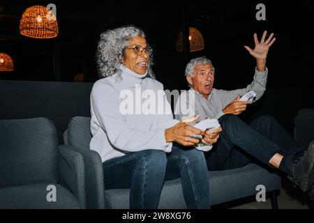 Uomo anziano felice che gioca a videogame con un'amica al centro giochi Foto Stock