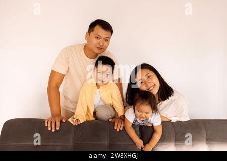 Felice famiglia asiatica a casa. Una coppia coreana e i loro piccoli bambini adorabili sul divano del soggiorno. I genitori, i loro figli e la loro figlia posano insieme Foto Stock