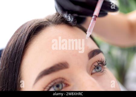 Iniezioni di bellezza. Una cosmetologa donna con guanti neri fa un'iniezione al suo cliente. Trattamento con acido ialuronico. Introduzione di liquido in Foto Stock