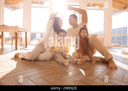 I genitori asiatici fanno un tetto simbolico di mani sopra i loro bambini carini. Famiglia felice con bambini piccoli goditi il trasloco in una nuova casa. Mamma, papa', da Foto Stock