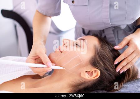 Medico che controlla la pelle della faccia della donna nella clinica di cosmetologia prima dell'ambulatorio di plastica. Chirurgo o estetista che tocca la faccia della donna. Cliente femminile con lin facciale Foto Stock