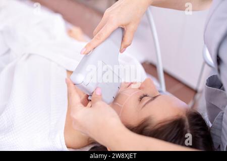 Ritratto di giovane donna rilassato ottenere SMAS ultrasuoni viso sollevamento massaggio con attrezzature professionali in centro di bellezza Foto Stock