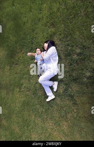 Mamma sorridente asiatica e dolce figlia sono sdraiati su un prato verde. Un'affascinante donna coreana e il suo bambino carino si stanno divertendo sull'erba. Una giovane madre A. Foto Stock