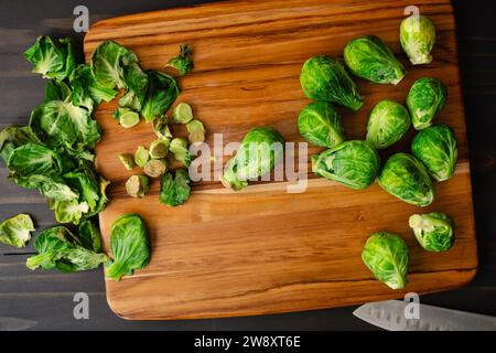 Cavoletti di Bruxelles tagliati su un tagliere di legno: Cavoli pelati e tagliati con foglie e steli su un tagliere di legno Foto Stock