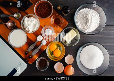 Ingredienti misurati e pesati della torta al cioccolato: Vista dall'alto degli ingredienti della torta nei recipienti di preparazione con misurini, separatore di uova e bilancia Foto Stock