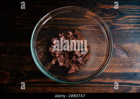 Cioccolato semi-dolce tritato in una ciotola di miscelazione in vetro: Vista dall'alto di pezzi di cioccolato da forno in una ciotola resistente al calore Foto Stock