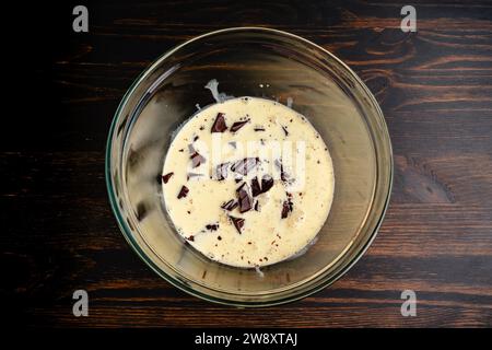 Preparazione del ganache di cioccolato in una ciotola di miscelazione in vetro: Cioccolato semidolce tritato che si scioglie in una panna pesante riscaldata Foto Stock