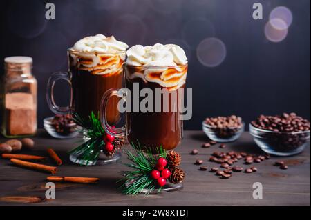 Caffè natalizio speziato condito con panna montata: Due tazze in vetro di caffè speziato appena fatto con decorazioni e ingredienti natalizi Foto Stock