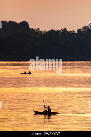 Sagome di persone che camminano in kayak attraverso le calme acque del Mekong, nell'arcipelago si Phan Don, attraverso raggi di luce dorata riflessa dal riv Foto Stock