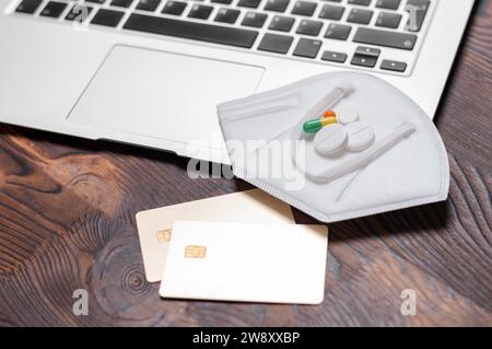 Immagine di un computer portatile, una carta d'oro, pillole e dispositivi di protezione contro il coronavirus. Concetto di assicurazione sanitaria. La medicina. Supporti misti Foto Stock