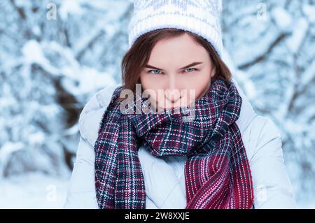 Ritratto di una donna affascinante con un'espressione scontenta sullo sfondo di alberi innevati. Concetto natalizio. Supporti misti Foto Stock