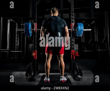 L'atleta professionista si trova di fronte ai bar con un campanello e sta per accovacciarsi con lei. Vista posteriore Foto Stock