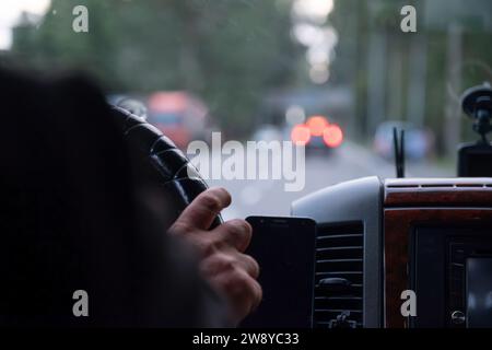 le mani di un vecchio mentre si guida su strada con luci sfocate e traffico automobilistico Foto Stock