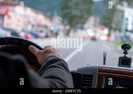 le mani di un vecchio mentre si guida su strada con luci sfocate e traffico automobilistico Foto Stock