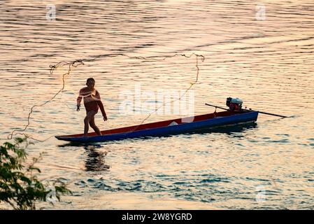 4000 isole, Laos-02 febbraio 2023: Sagoma di un pescatore, che getta una rete dalla sua stretta barca, vicino al tramonto, sulle acque del fiume vicino a Don D. Foto Stock
