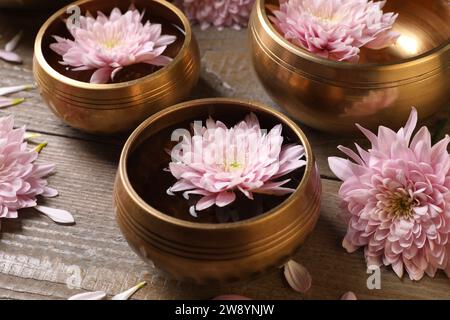 Ciotole tibetane con acqua e bellissimi fiori su un tavolo di legno, primo piano Foto Stock