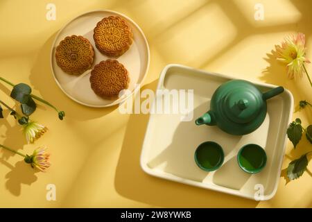 Layout minimale e semplice: Torte lunari, set da tè e fiori su sfondo giallo per il Mid-Autumn Festival. Vista dall'alto. Scena pubblicitaria. Cinese Mid-Au Foto Stock
