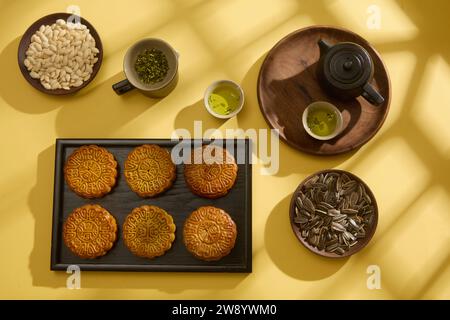 La Mooncake è una torta tradizionale durante il festival di metà autunno, collocata su un vassoio nero esposto con piatti di semi di zucca e semi di girasole su sfondo giallo Foto Stock