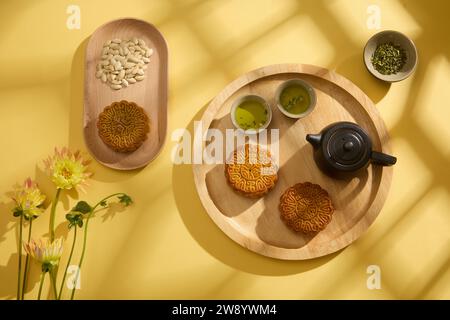 Concetto di tradizionale cibo cinese da festival su un asiatico. Su sfondo giallo, vassoi di legno contenenti torte lunari, set di tè e decorazioni con semi di zucca Foto Stock