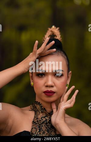 Volto coraggioso di una donna asiatica in costume verde tradizionale con accessori dorati sul suo corpo durante il concorso in un festival di danza di fronte a Foto Stock