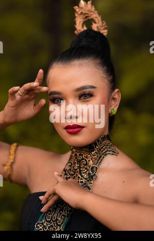 Ritratto di una donna asiatica con trucco e labbra rosse mentre indossa una collana dorata e accessori dorati sui capelli neri mentre si trova di fronte Foto Stock