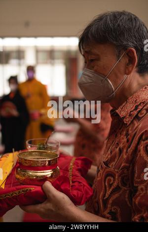 Bandung, Indonesia - 8 gennaio 2022: Il vecchio porta le offerte all'altare mentre prega con i monaci all'interno del tempio del Buddha Foto Stock