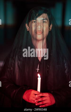 un adoratore del diavolo maschio con un velo trasparente sta eseguendo un rituale spettrale tenendo una candela in mano la notte Foto Stock