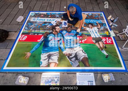 Un artista utilizza il gesso per disegnare un quadro generale dei calciatori del Napoli SSC, che hanno appena vinto il campionato italiano nel 2023, in strada. Foto Stock