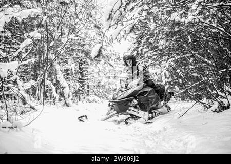 Pilota su una motoslitta sportiva in una foresta di montagna. L'atleta cavalca una motoslitta in montagna. Motoslitta sulla neve. Sport invernali di concetto Foto Stock