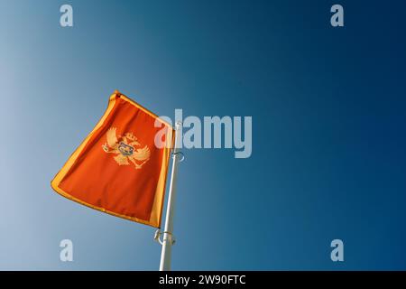 La bandiera del Montenegro fluttua su un'asta bianca contro un cielo blu Foto Stock