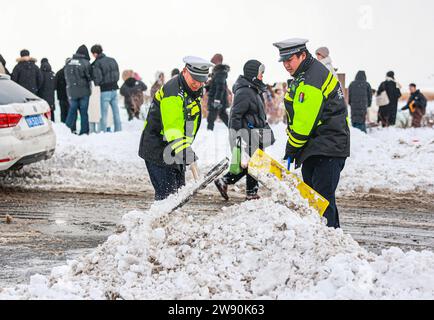 Pechino, provincia cinese di Shandong. 22 dicembre 2023. Gli agenti di polizia puliscono la neve su una strada vicino al lago dei cigni a Rongcheng, nella provincia dello Shandong della Cina orientale, 22 dicembre 2023. Sono state adottate contromisure per prevenire o alleviare gli impatti causati da nevicate estese e altre condizioni di congelamento. Crediti: Li Xinjun/Xinhua/Alamy Live News Foto Stock