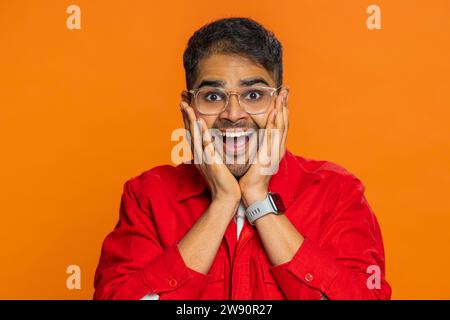 Oh mio Dio, wow. Entusiasta e stupito uomo vincitore che alza le mani di sorpresa guardando la fotocamera con grandi occhi, scioccato dall'improvvisa vittoria che celebra il successo ottenuto buone notizie. Ragazzo su sfondo arancione Foto Stock