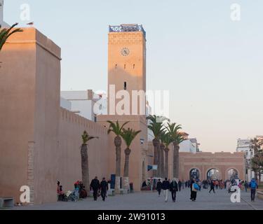 Strada principale con torre dell'orologio piena di gente la sera a Essaouira, Marocco. 22 dicembre 2023 Foto Stock