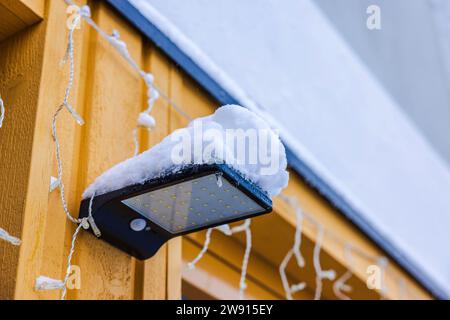 Vista ravvicinata della luce esterna con pannello solare innevato sulla facciata della villa nelle gelide giornate invernali. Foto Stock