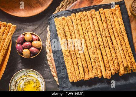 Deliziosi grissini grissini con erbe fresche in cima. Servito con olive sott'aceto e salsa cremosa con gocce di olio d'oliva e timo fresco. Foto Stock