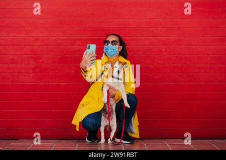 Donna che indossa la maschera facciale che fa selfie con il cane Foto Stock