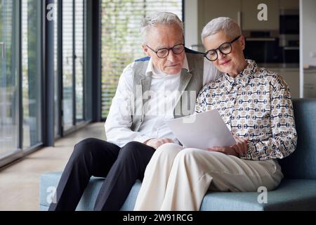 Coppia anziana seduta sul divano a casa a leggere un documento Foto Stock