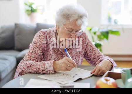 Donna anziana con la penna che fa un puzzle di parole incrociate nel libro a tavola Foto Stock